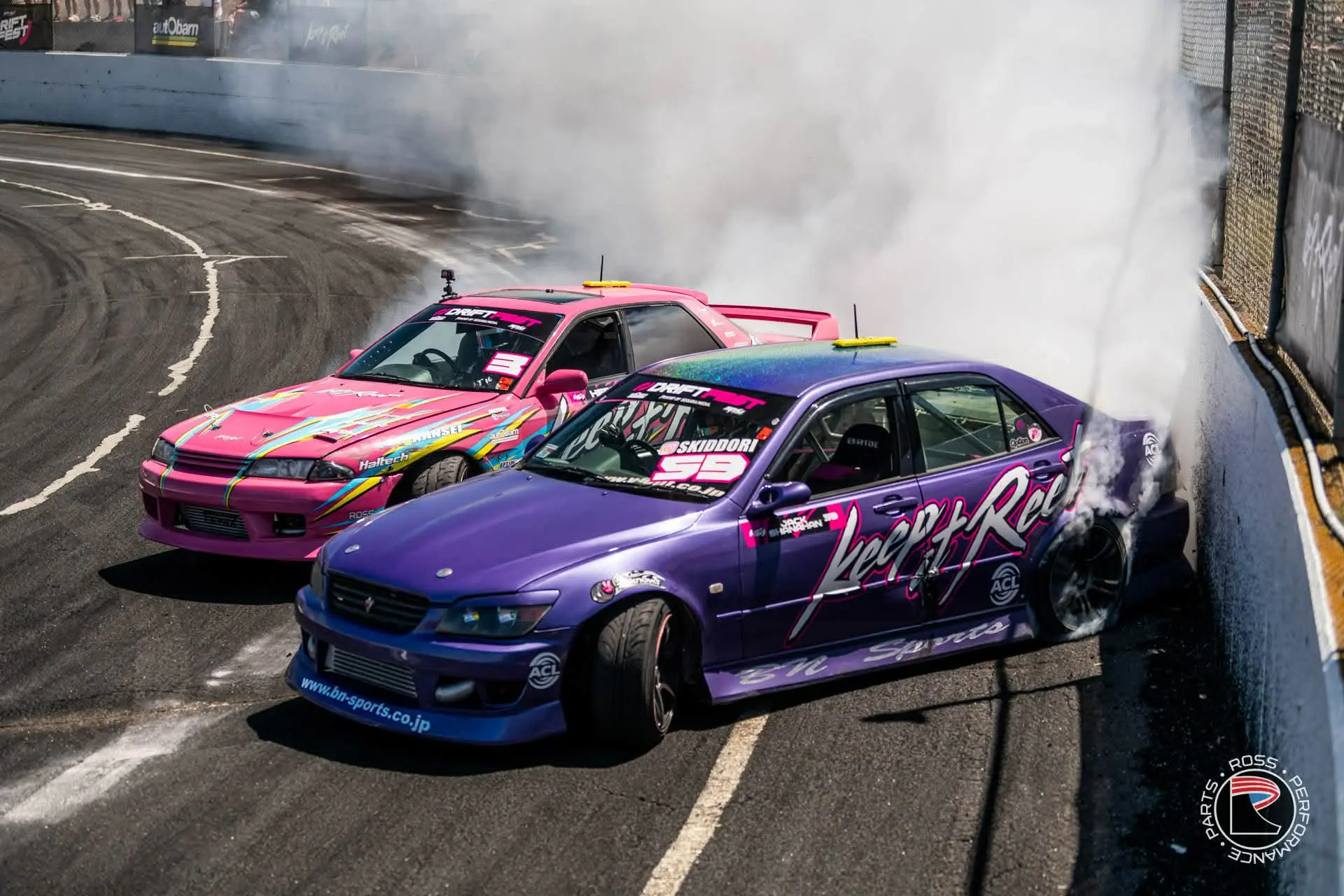 Two Ross Performance Parts-supported drift cars driving in tandem through heavy tyre smoke