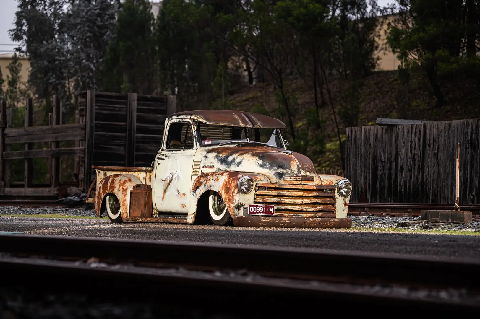 Patina-covered custom truck photographed beside railway tracks