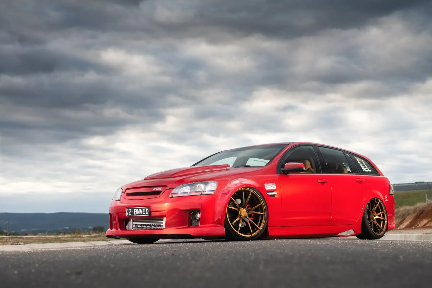 Red modified performance wagon photographed beneath a dramatic sky