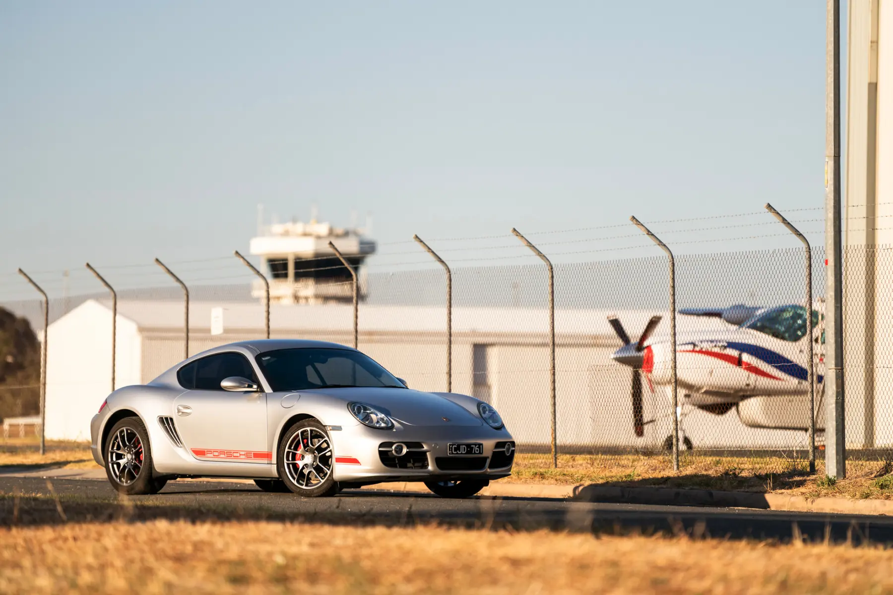 Silver Porsche Cayman photographed beside an aircraft